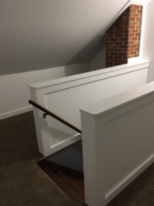 A renovated staircase with white railings and a wooden handrail leading to a basement by Casco Bay Construction Services, LLC in South Portland, ME.