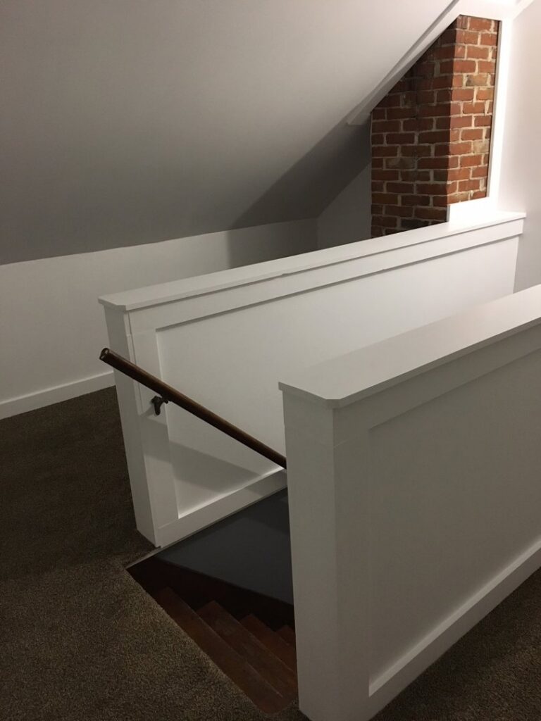 A renovated staircase with white railings and a wooden handrail leading to a basement by Casco Bay Construction Services, LLC in South Portland, ME.