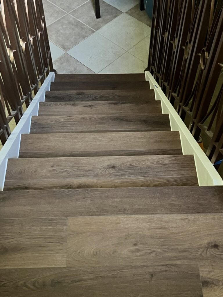 A renovated staircase with dark wood-look treads and ornate metal railings, a project by SD Masters in Miami, FL.