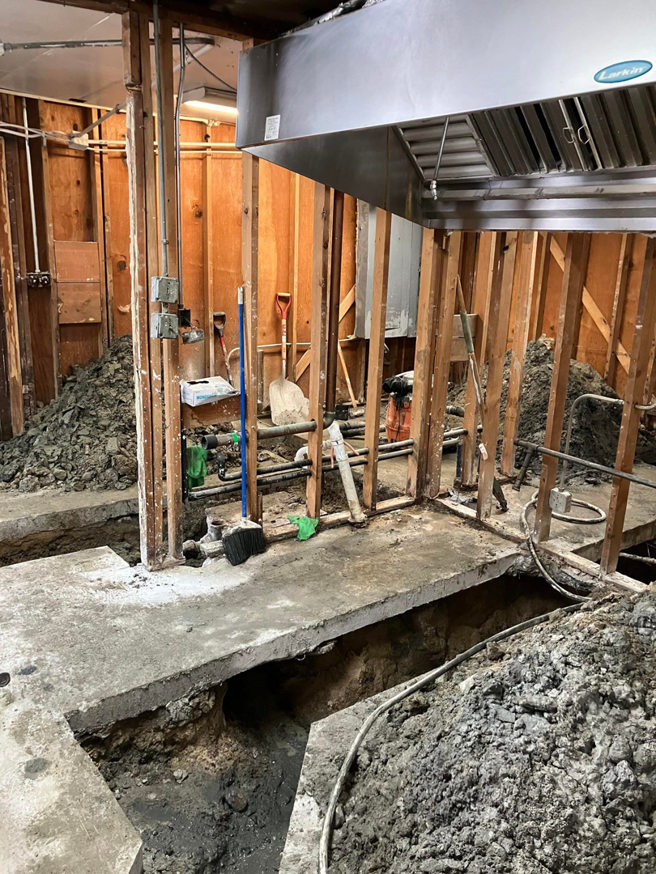 A renovation area with exposed studs, floor trenches, and a commercial hood by JB Renovations in Houston, TX.