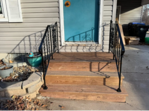 A newly repaired front porch with wooden steps and black metal railings installed by Bill's Handyman Services in Anchorage, AK.