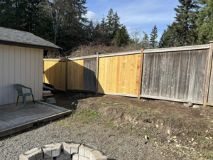 View of a backyard wooden fence with new and old sections, indicating repair work by HandyMan Shocks in Tacoma, WA.