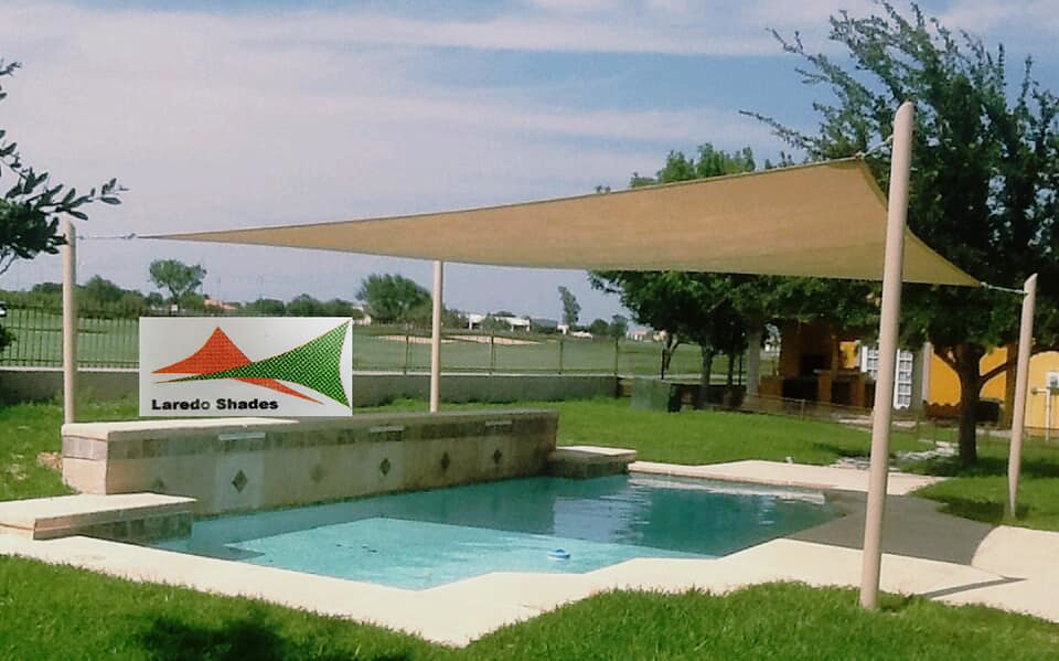 A tan shade sail installed over a residential backyard pool by Laredo Shades, a general contractor in Laredo, TX.