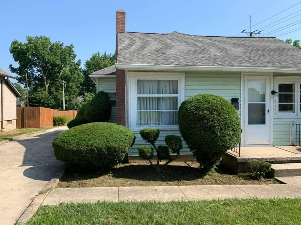 A residential front yard with decorative trimmed bushes and landscaping by E&K Property Preservation in Lake, MI.