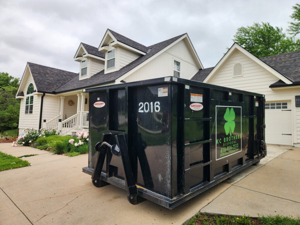 A black KC Brothers Disposal dumpster parked in a residential driveway for waste removal in Kansas City, MO.