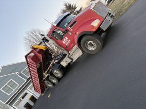 A Geppert Recycling truck delivering a red dumpster to a residential driveway for junk removal in Philadelphia, PA.