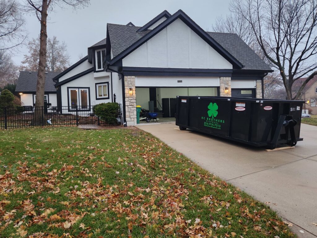 A black KC Brothers Disposal dumpster delivered to a residential driveway for junk removal in Kansas City, MO.