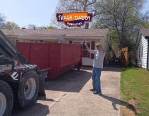 A red dumpster being delivered or picked up at a residential driveway by Trash Daddy in Fort Worth, TX