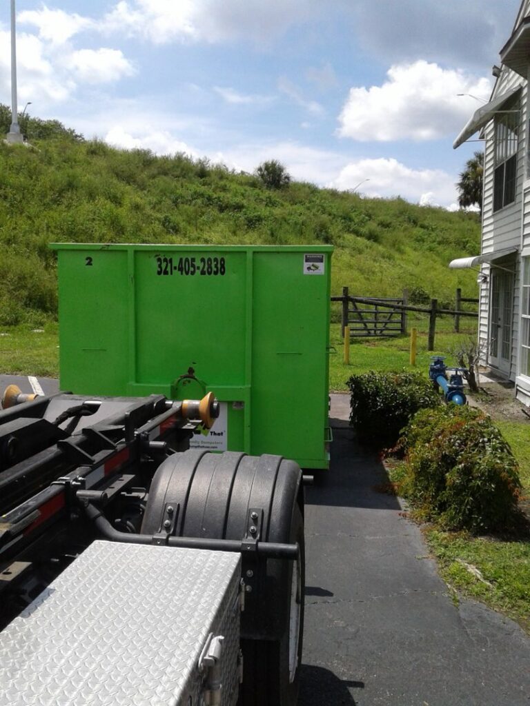 A green dumpster being delivered to a residential driveway for junk removal service by Bin There Dump That Dumpster Rental Orlando, FL.