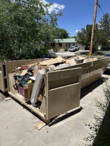 A large dumpster from Bin Suave LLC filled with household junk and debris in a residential driveway in Espanola, NM.