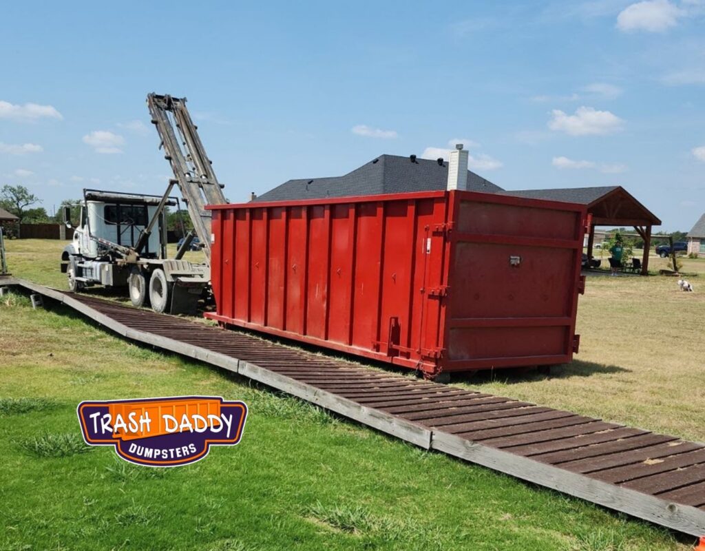 A Trash Daddy truck picking up a red dumpster from a residential property in Fort Worth, TX