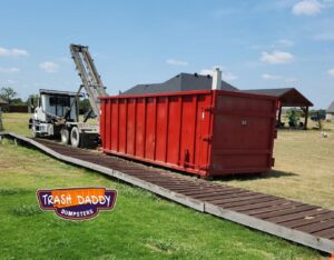 A Trash Daddy truck picking up a red dumpster from a residential property in Fort Worth, TX