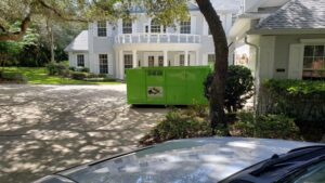 A green dumpster placed in a residential driveway for junk removal by Bin There Dump That Dumpster Rental Orlando, FL.