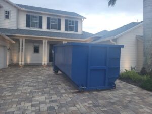 An empty blue dumpster placed on a residential driveway for junk removal by R&Y Dumpster Kings in Tampa, FL.