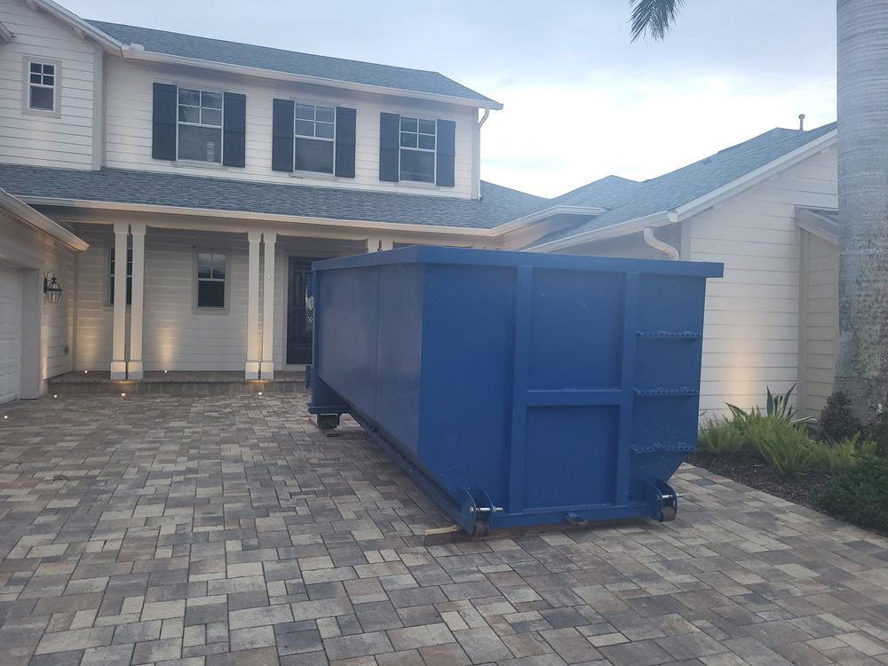 An empty blue dumpster placed on a residential driveway for junk removal by R&Y Dumpster Kings in Tampa, FL.