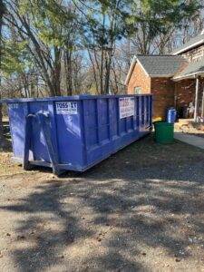 A Toss-It dumpster parked on a residential driveway for home cleanout or renovation in Glen Burnie, MD.