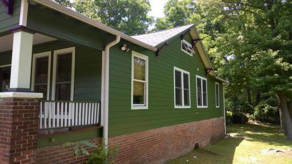 The side exterior of a residential home with green siding and brick foundation by Randolph Residential Repair in Durham, NC.