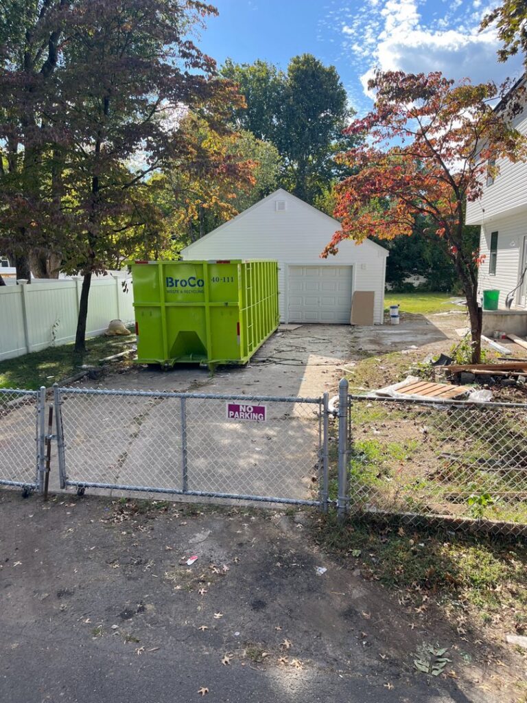 A green Broco Waste & Recycling dumpster in a residential driveway for a garage cleanout in Warminster, PA.
