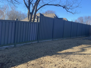 A sturdy grey privacy fence installed in a residential backyard, showcasing work by Aaron Fence in Tulsa, OK.
