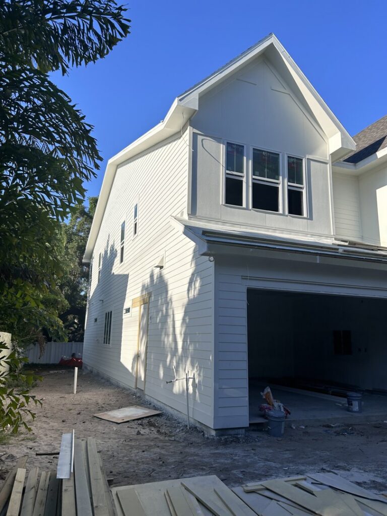 Residential home construction showing white siding installation and an open garage by M&J Florida Enterprise Llc in Orlando, FL.