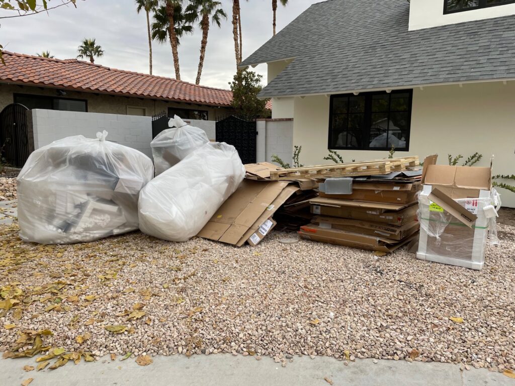 Piles of cardboard boxes and white trash bags outside a residential property, ready for junk removal by Gone Junkin' Vegas in Henderson, NV.