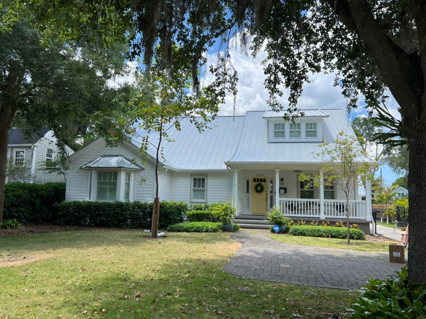 A charming white house with a newly installed white metal roof, showcasing a completed project by Hastings Roofing Service Inc. in Orlando, FL.