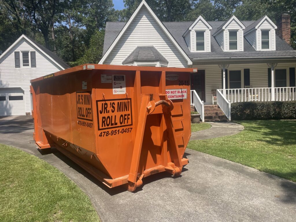 An orange roll-off dumpster from Jr's Mini Roll Off LLC placed in a residential driveway in Byron, GA.