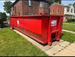 A large red roll-off dumpster from The Dump Town placed on a residential driveway in Detroit, MI.