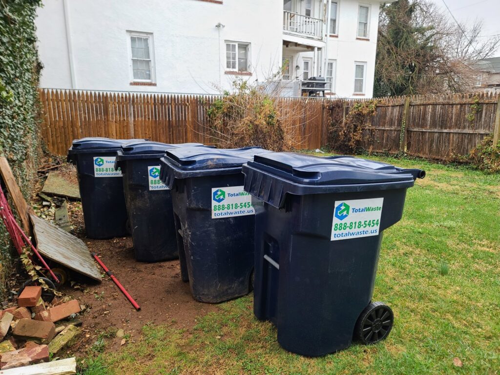 Four residential trash bins with Total Waste branding lined up in a grassy backyard in Baltimore, MD.
