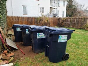 Four residential trash bins with Total Waste branding lined up in a grassy backyard in Baltimore, MD.