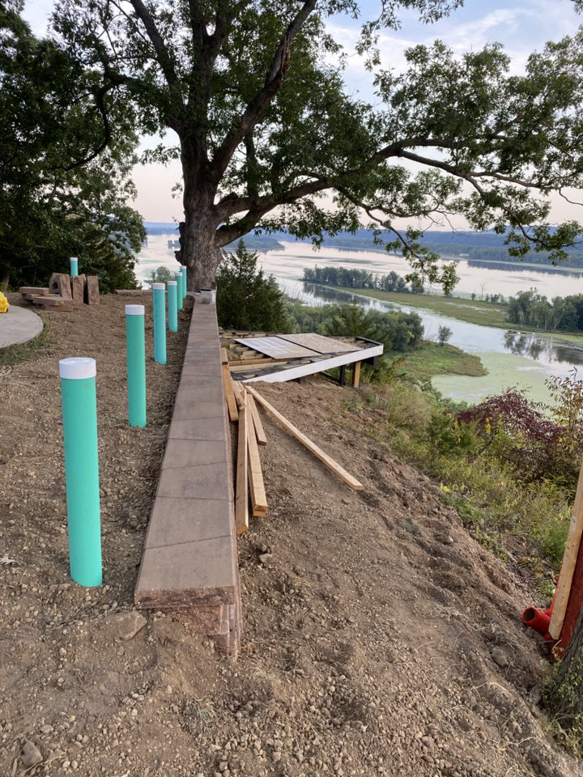 A retaining wall and landscaping structure under construction on a sloped property overlooking water by Building Arts by Jimmy Z in Cassville, WI.