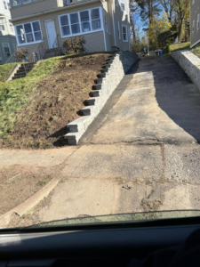 Newly installed stone retaining wall and steps alongside a driveway by Juan M Construction LLC in Waterbury, CT.