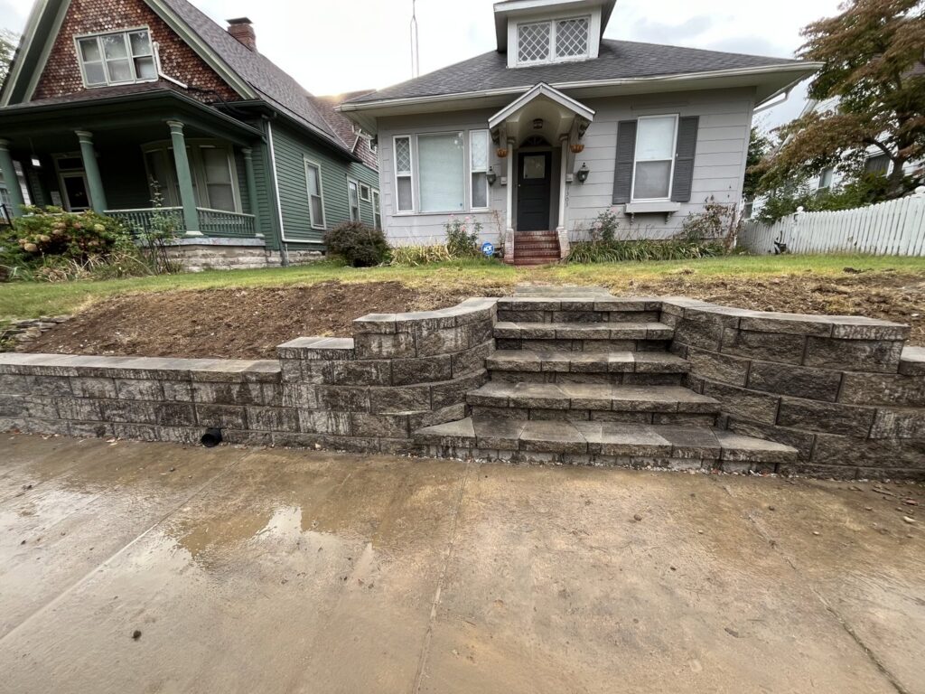 A newly installed stone retaining wall with integrated steps leading to a house by Lankford Dirt Works LLC in Indianapolis, IN.