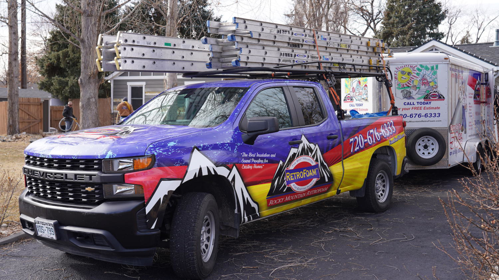 A Rocky Mountain RetroFoam work truck with ladders and a trailer parked at a home in Denver, CO, ready for a handyman job.