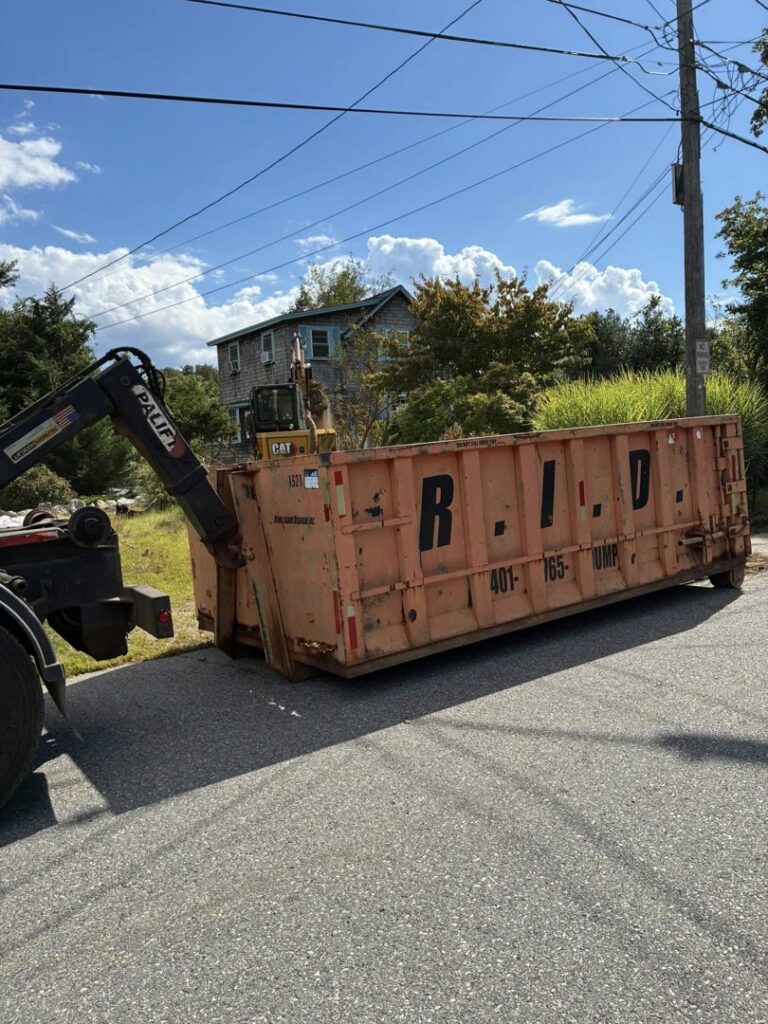 A Rhode Island Disposal truck deploying a roll-off dumpster on a residential street for junk removal in Providence, RI.