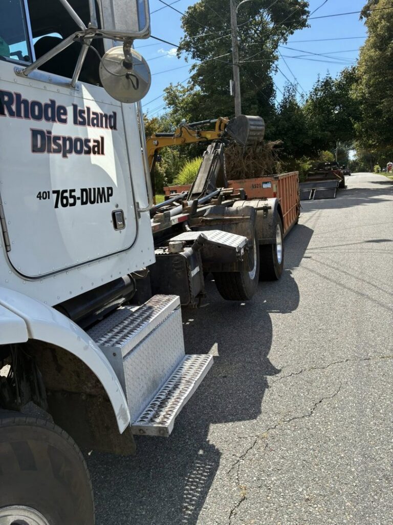 A Rhode Island Disposal truck with a dumpster being loaded with debris by an excavator during a junk removal job in Providence, RI.