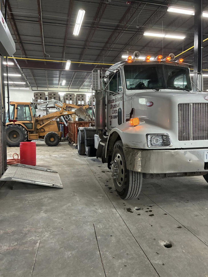 Rhode Island Disposal truck and a backhoe next to a roll-off dumpster in a facility in Providence, RI.