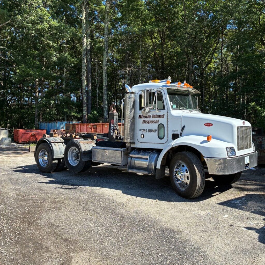 A Rhode Island Disposal roll-off truck parked in a yard with multiple empty dumpsters in Providence, RI.