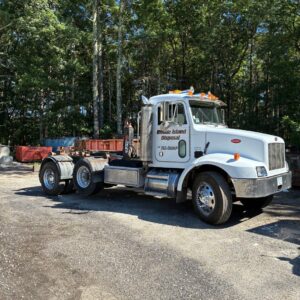 A Rhode Island Disposal roll-off truck parked in a yard with multiple empty dumpsters in Providence, RI.