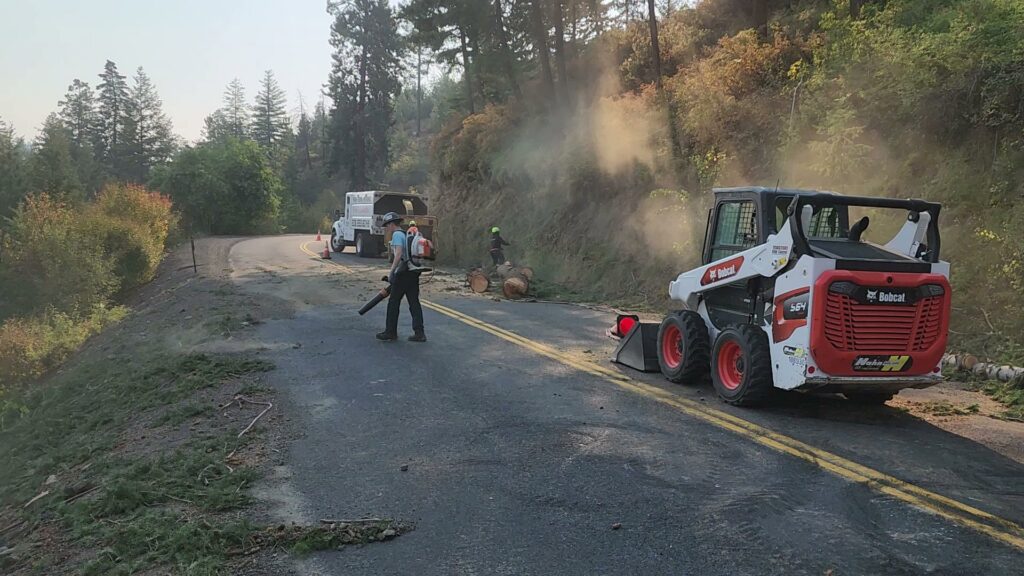 Workers clearing tree debris from a road with a Bobcat skid-steer and chipper truck for D&R Tree Service in Lewiston, ID.