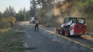 Workers clearing tree debris from a road with a Bobcat skid-steer and chipper truck for D&R Tree Service in Lewiston, ID.