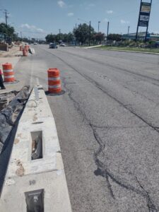 A road construction site with concrete barriers and orange traffic barrels, indicating ongoing work by Zachry Construction Corporation in San Antonio, TX.
