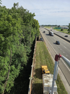 Roadside tree trimming and clearing along a highway, performed from a bucket truck by M.L tree service in Dayton, OH.