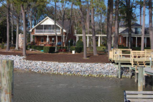 A waterfront home with a protective rock revetment and a wooden dock, constructed by Spence Marine Construction Inc. in Virginia Beach, VA.