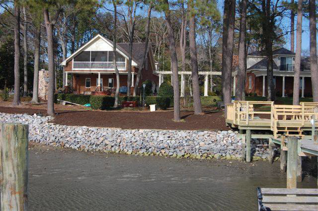 A waterfront home with a protective rock revetment and a wooden dock, constructed by Spence Marine Construction Inc. in Virginia Beach, VA.