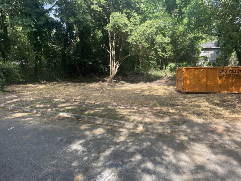 An orange roll-off dumpster from Jr's Mini Roll Off LLC on a recently cleared lot in Byron, GA.