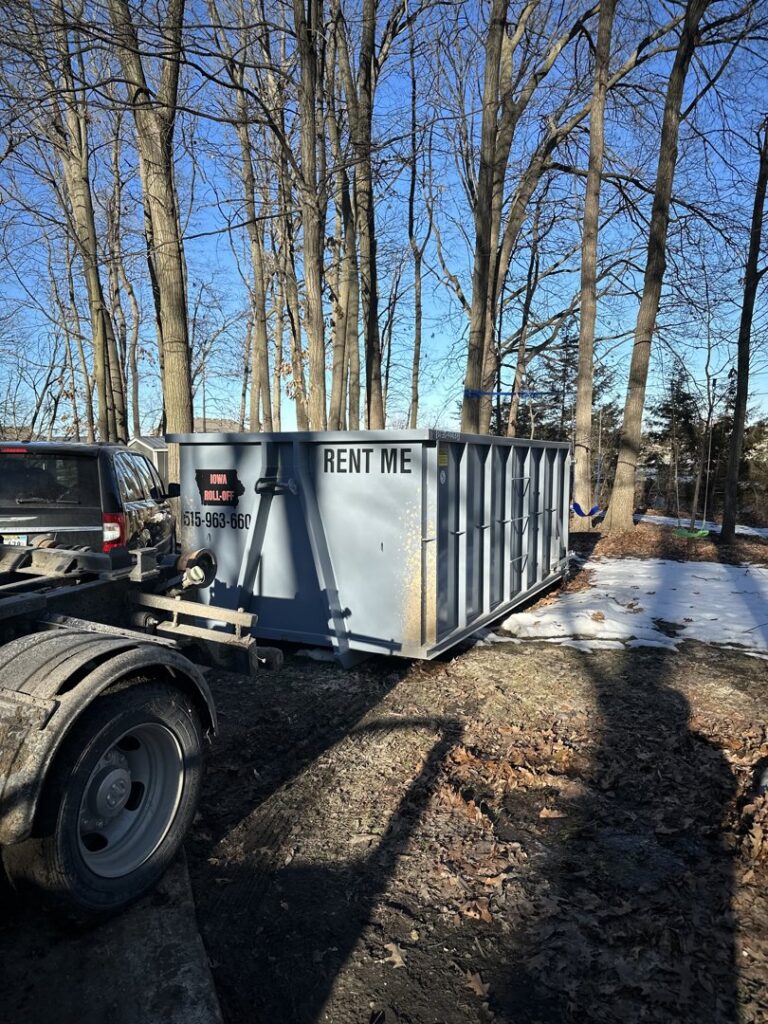 A roll-off dumpster being delivered or picked up by a truck in a wooded area by Iowa Roll Off in Ankeny, IA.