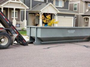 A Thomas Roll-Off truck delivering a large grey roll-off dumpster for general junk removal service in Akron, OH.