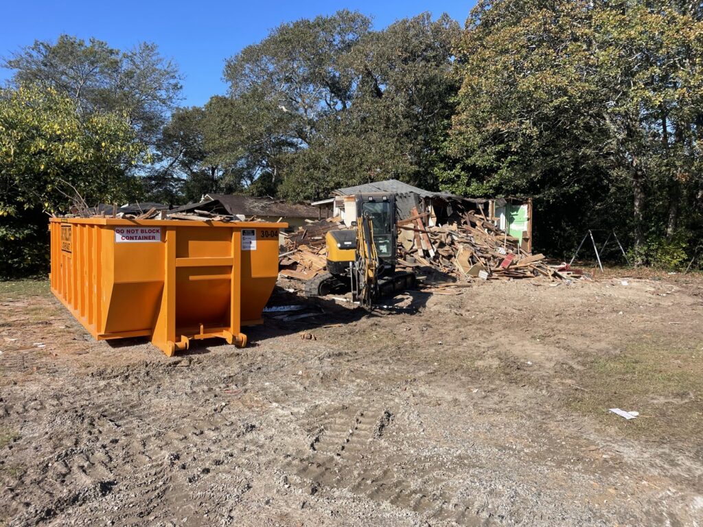 An orange roll-off dumpster from Jr's Mini Roll Off LLC at a demolition site with debris in Byron, GA.