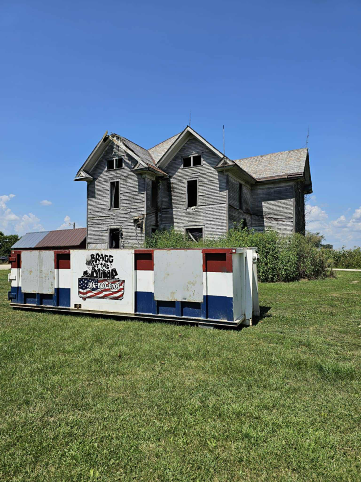 A large roll-off dumpster from Bragg About This Dump placed in front of a dilapidated house in Columbus, OH.